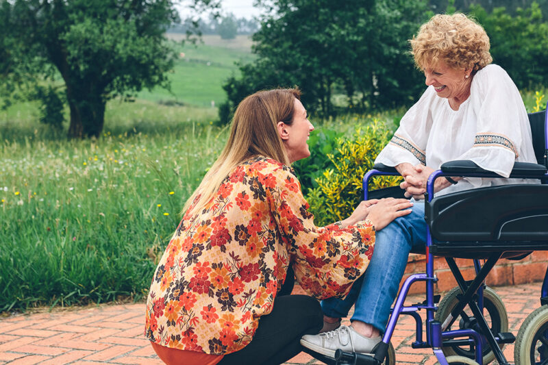 Affectionate young woman talking to elderly woman in a wheelchair in the garden