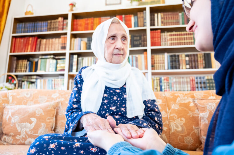 Happy arabic muslim granddaughter holding her grandmother hands